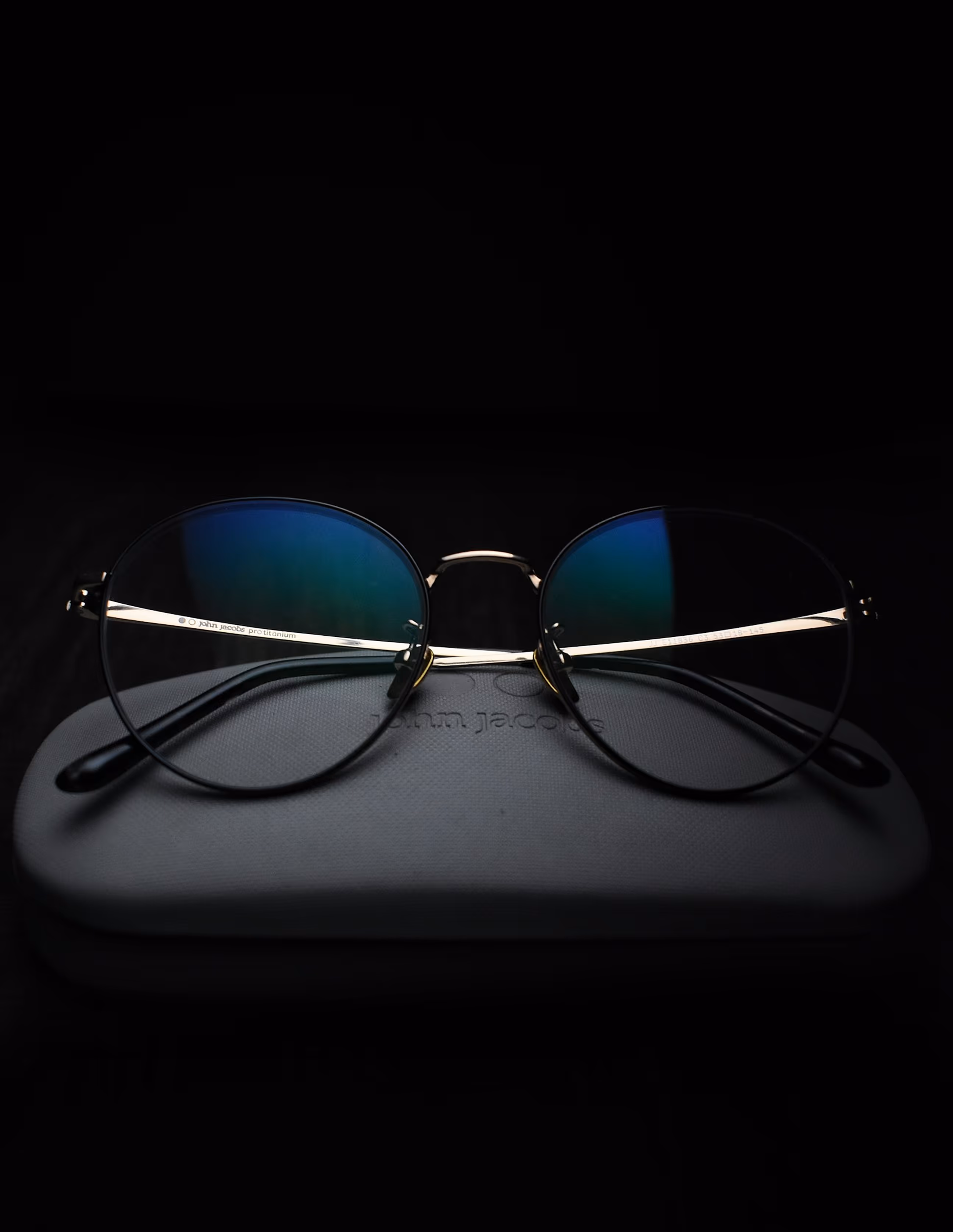 Round metallic eyeglasses with blue-tinted lenses resting on a gray textured case.