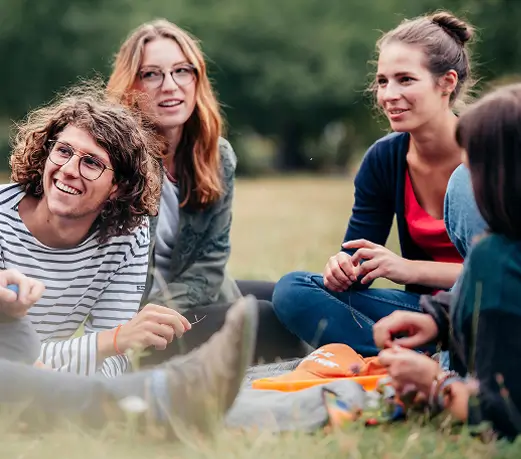 Vier junge Menschen sitzen im Gras im Freien und unterhalten sich entspannt.