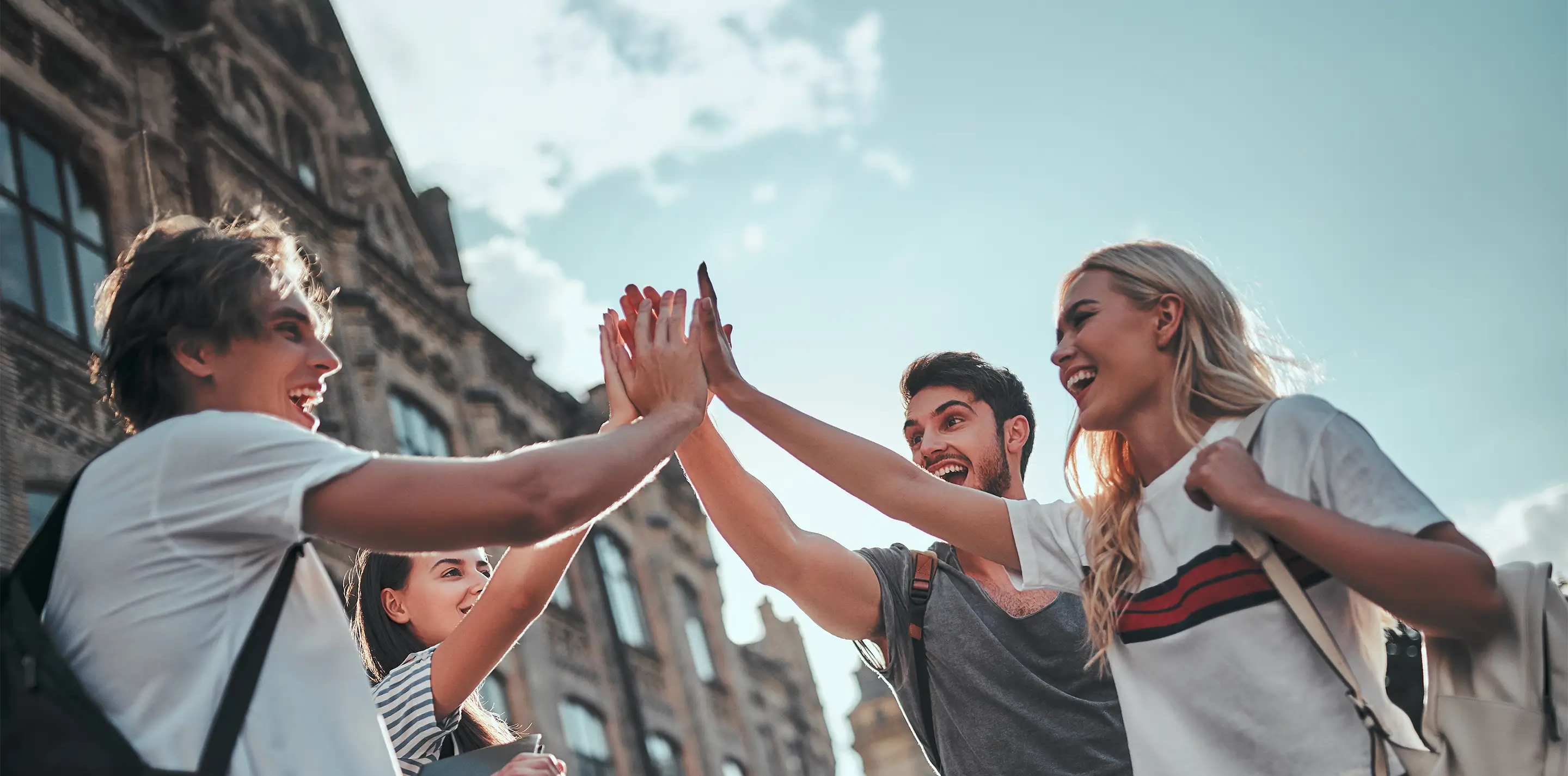 Vier Studierende geben sich vor einem historischen Gebäude ein High Five und freuen sich über die finanzielle Unterstützung.