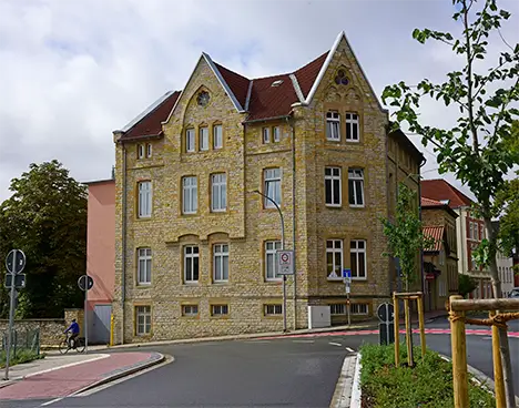 Wohnheim in der Ziegler Straße aus gelbem Backstein mit roten Ziegeldächern an einer abknickenden Straße, umgeben von Bäumen und begrünten Flächen.