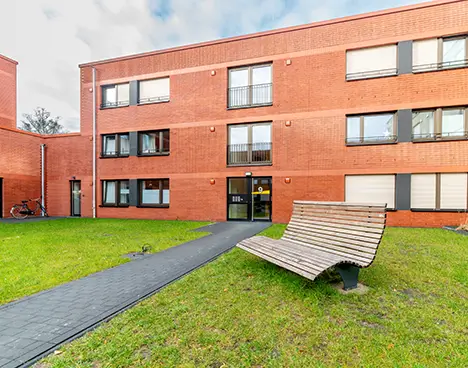 Moderne rote Backsteinwohngebäude mit gepflegtem grünen Rasen und einer geschwungenen Holzbank im Innenhof.