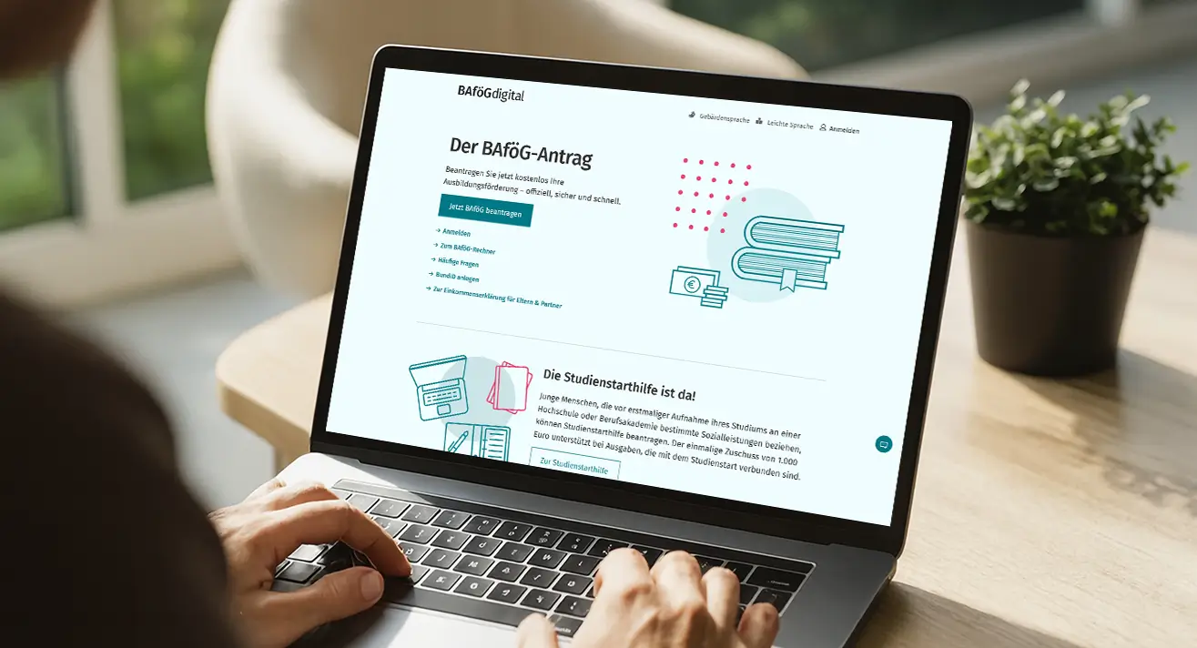 Der Schulterblick auf einen Laptop zeigt eine Webseite zum digitalen BAföG-Antrag mit Text und Illustrationen. Die Person tippt auf der Tastatur.
