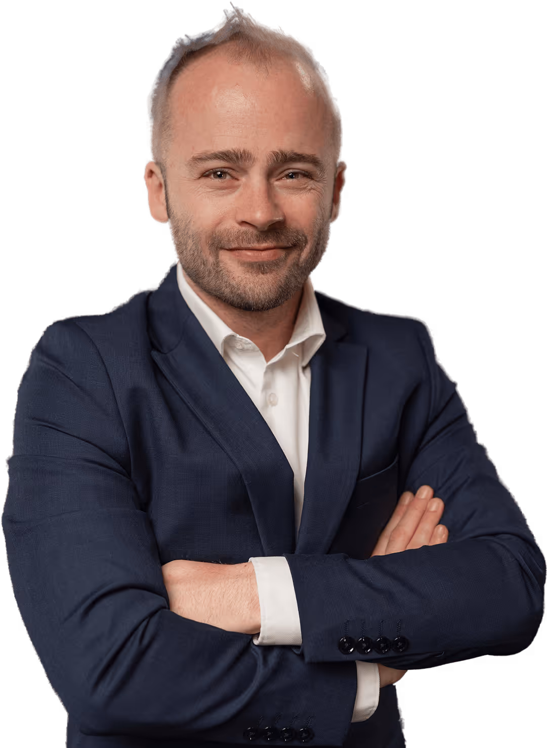 Muž v tmavě modrém obleku a bílé košili se založenýma rukama a mírným úsměvem.