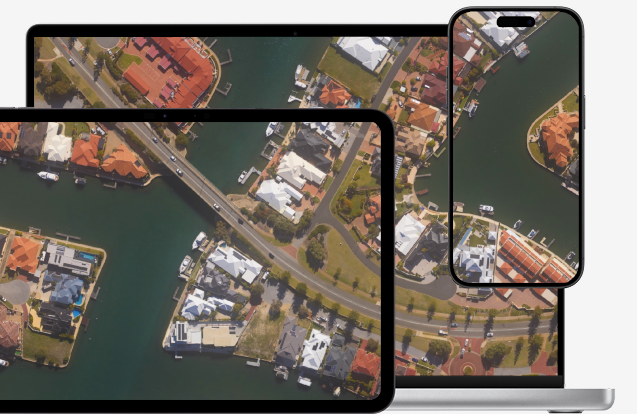Aerial view of a residential area with roads, houses, parked cars, and green spaces displayed on a smartphone, tablet, and laptop screens.