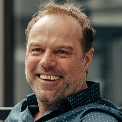 Middle-aged man with short hair and a beard smiling, wearing a dark blue shirt with white polka dots.