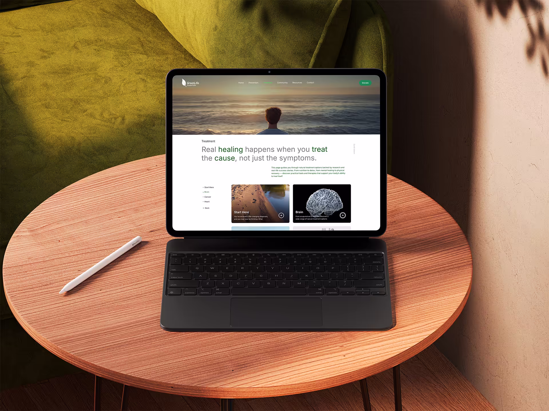 Tablet with keyboard on wooden table showing GreenLife website page about treatment with a background image of a person facing the ocean at sunset.
