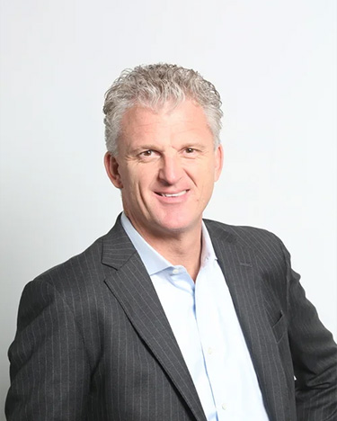 Smiling middle-aged man with gray hair wearing a dark pinstripe suit jacket and light blue shirt against a light background.