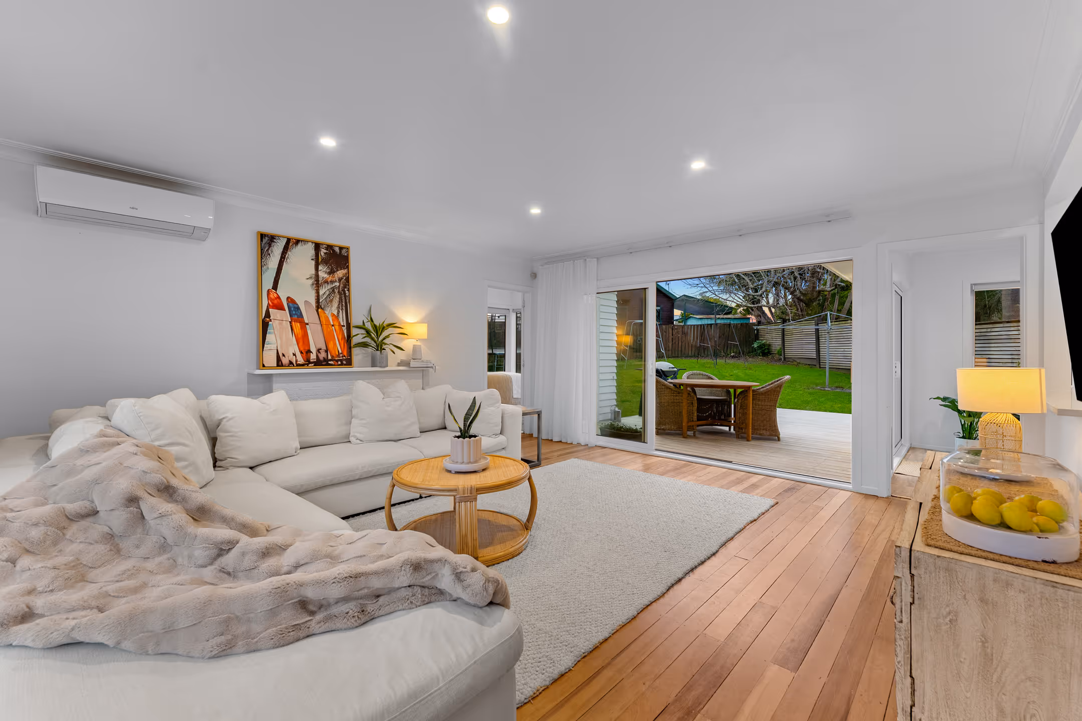 Modern living room with white sectional sofa, wooden floors, large sliding glass doors opening to a backyard patio with outdoor seating.