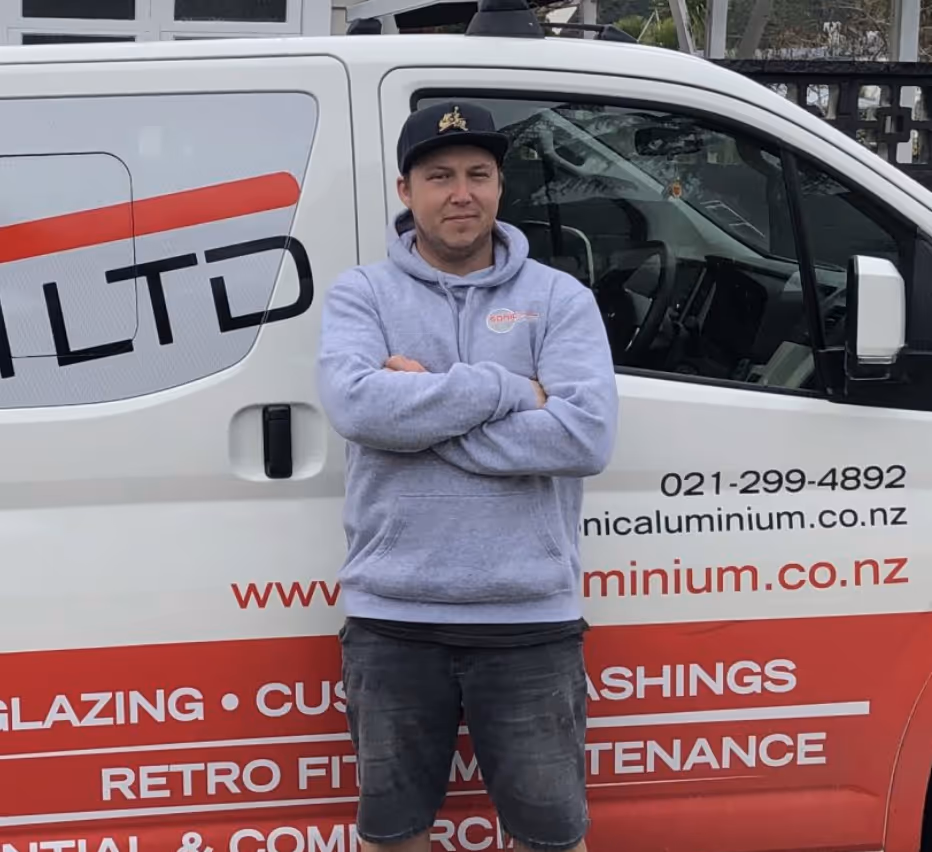 White house entrance with a porch, potted plant, welcome mat, and warm-lit windows showing a cozy living room inside.