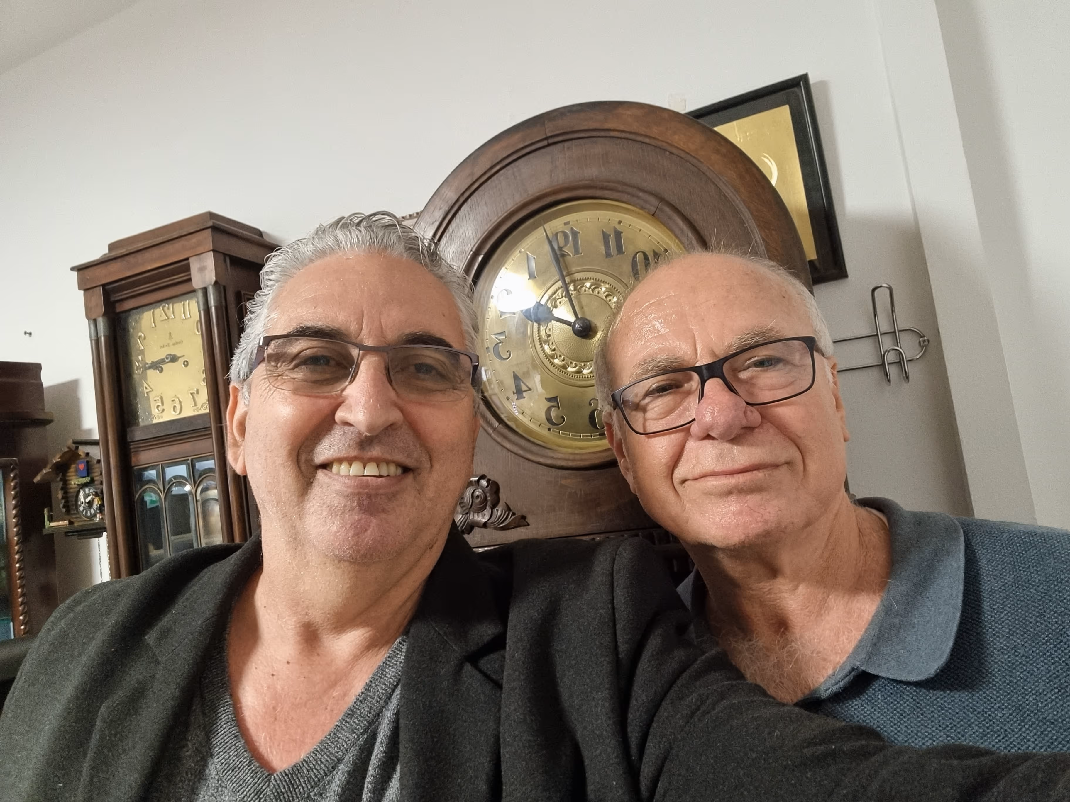 שני גברים מחייכים עם שעון עתיק גדול ברקע בבית.
