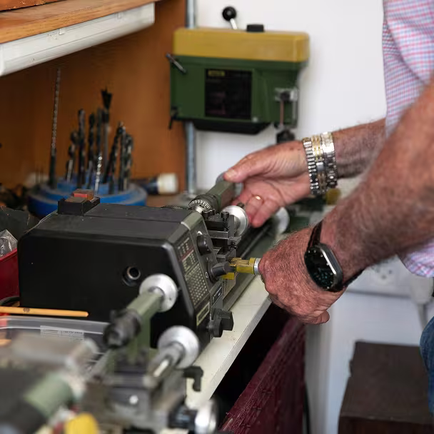 ידיים של אדם מתפעלת מכונת חריטה על שולחן עבודה לצד מקדחים ומכשירים.
