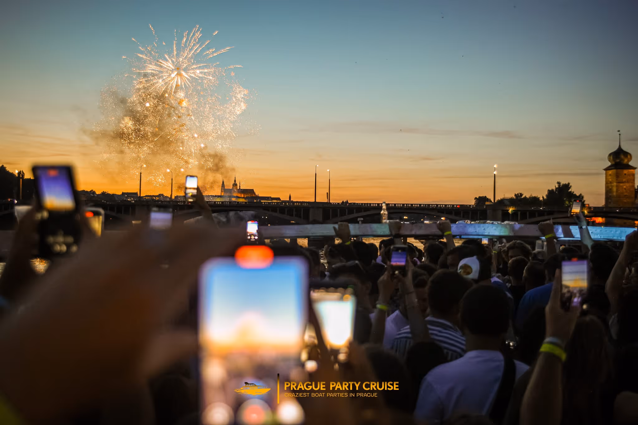 Crowd of people dancing and taking photos around a DJ performing in a dimly lit club with shelves of books on the walls.