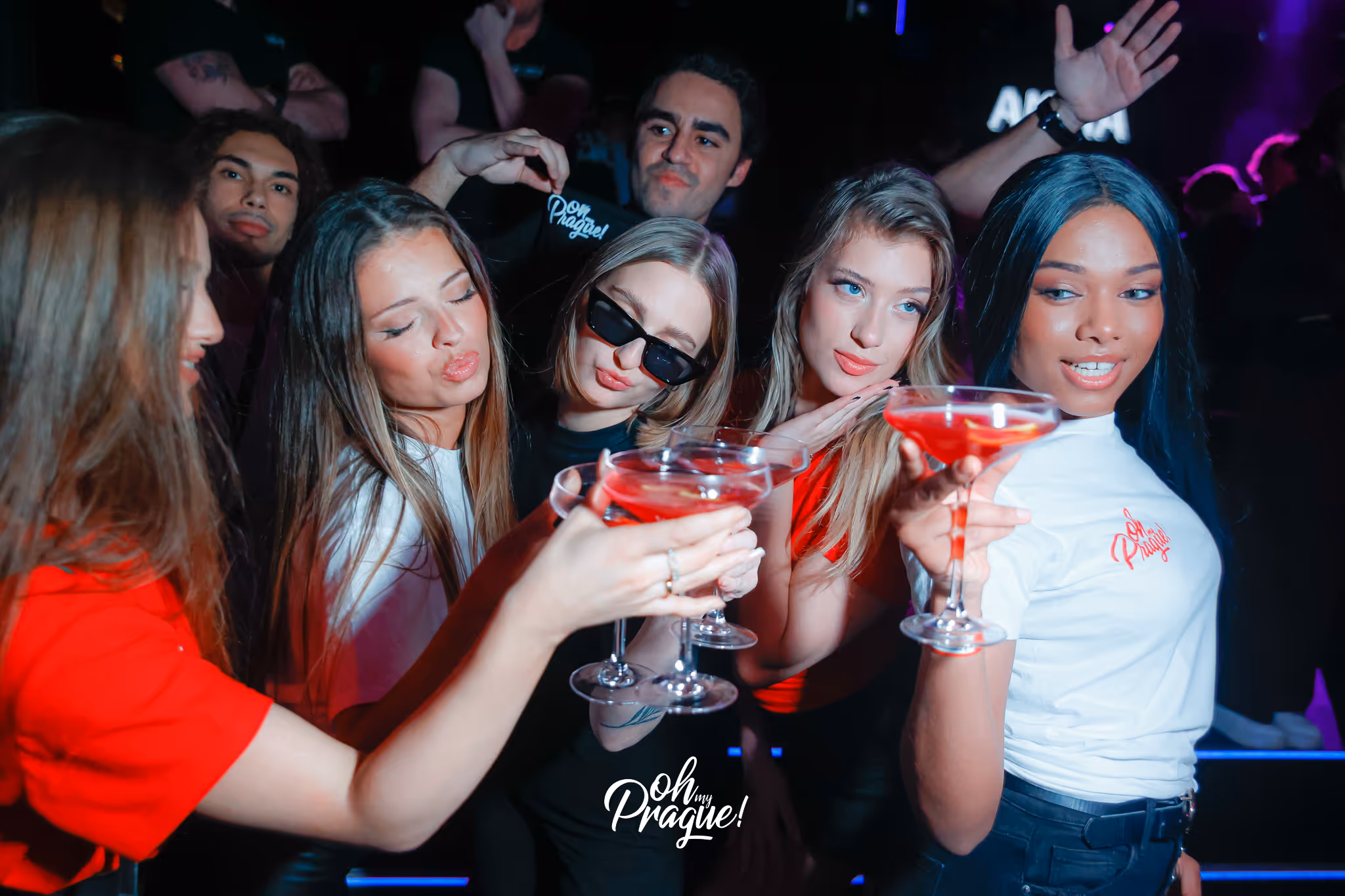 A group of five young people toasting with red cocktails and enjoying a night out in a club.
