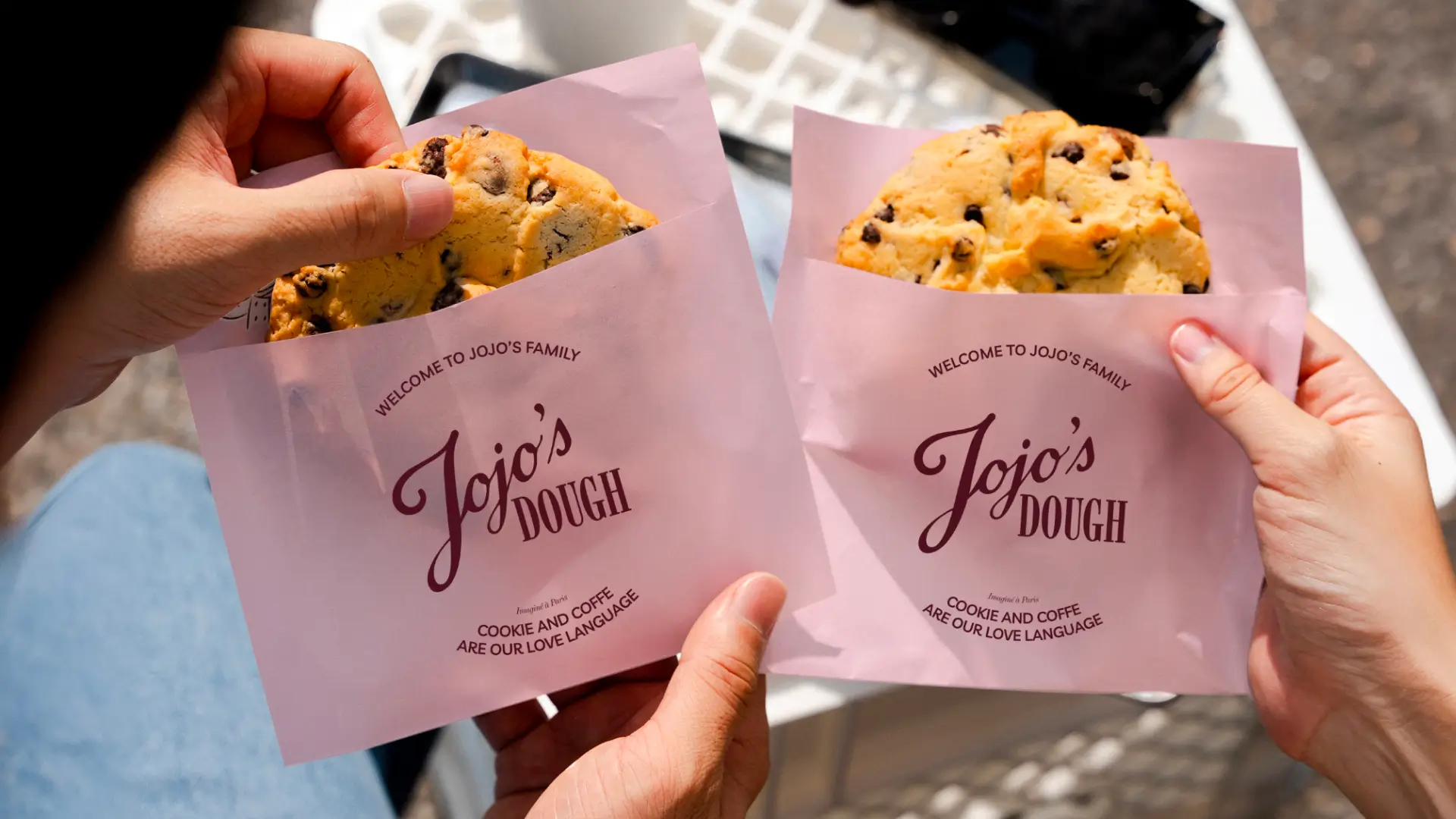 Cookies Jojo’s Dough servis dans des sachets roses logotypés, tenus en main en situation de dégustation