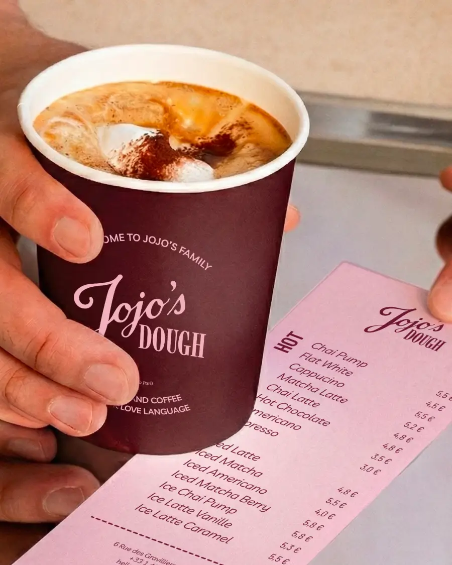 Boisson chaude servie dans un gobelet Jojo’s Dough, présentée avec la carte des boissons