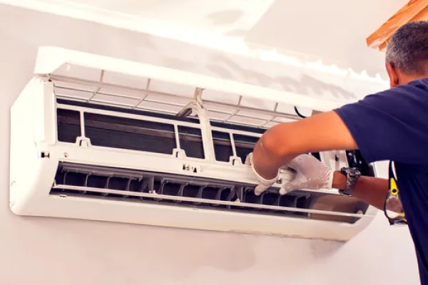 Technician wearing gloves servicing a wall-mounted air conditioning unit.