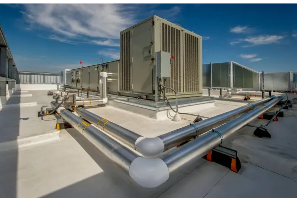 Large HVAC units and metal ventilation pipes installed on a flat rooftop under a partly cloudy blue sky.