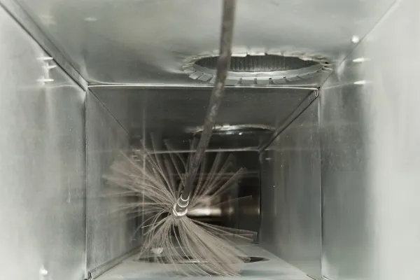 Inside view of a metal duct being cleaned with a rotating brush attached to a cable.