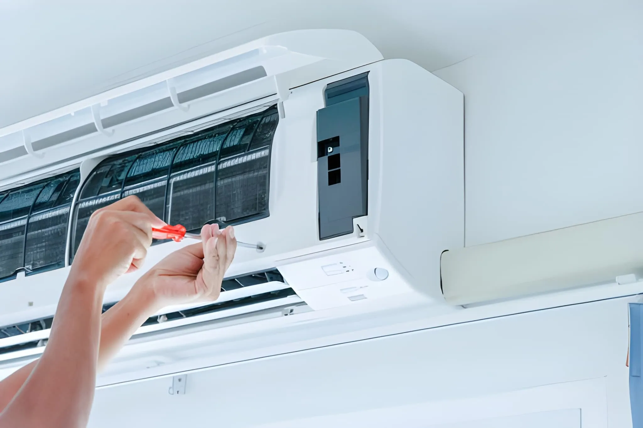 Hands using a screwdriver to repair the inside of a wall-mounted air conditioner unit.