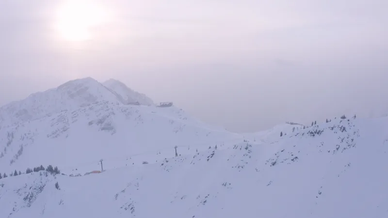 Snowy alpine terrain beneath pale winter sun and haze