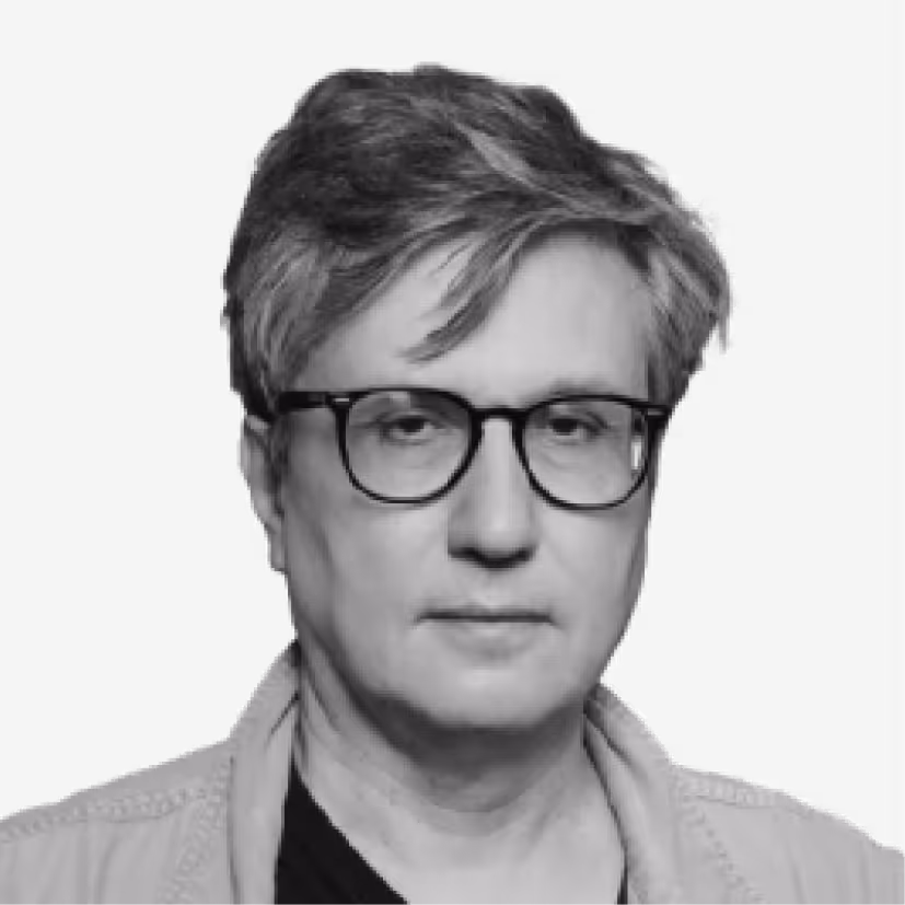 Middle-aged man with thick gray hair and black glasses wearing a light-colored jacket over a dark shirt against a black background.