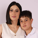 Woman with shoulder-length dark hair and light makeup standing next to a boy with short dark hair, both wearing white tops.