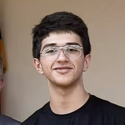 Young man with short dark hair and glasses smiling, wearing a black shirt.