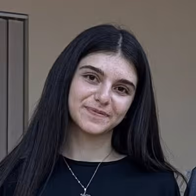 Young woman with long dark hair wearing a black top and a silver necklace, smiling gently.