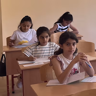 Four girls sitting at desks, focused on writing in a classroom.