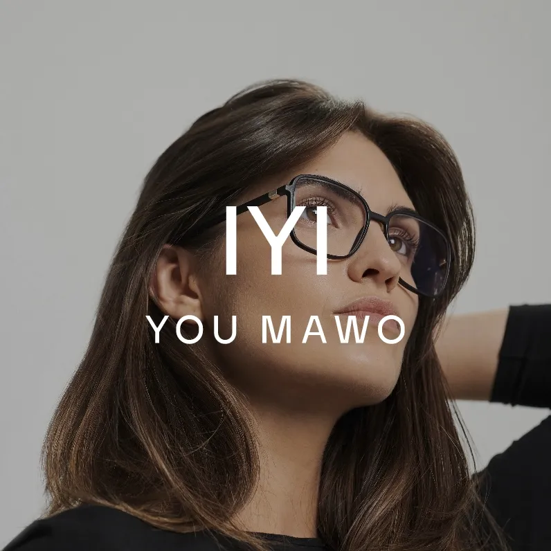 Markenbild You Mawo. Frau mit langen braunen Haaren trägt schwarze Brille und schaut nach oben vor grauem Hintergrund.