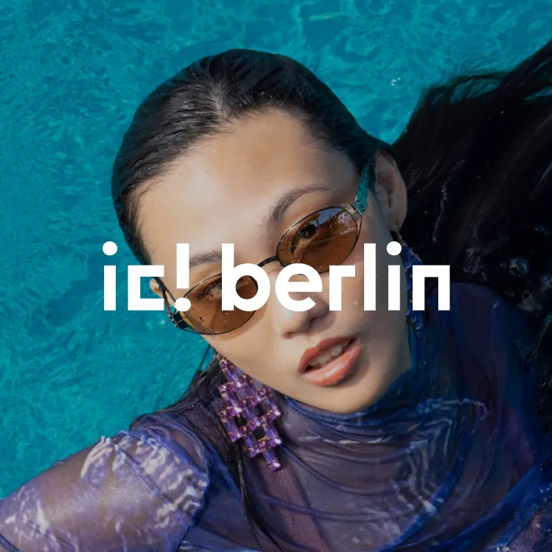 Markenbild ic! berlin. Frau mit braunen Sonnenbrillen und lila Ohrringen im blauen Wasser.
