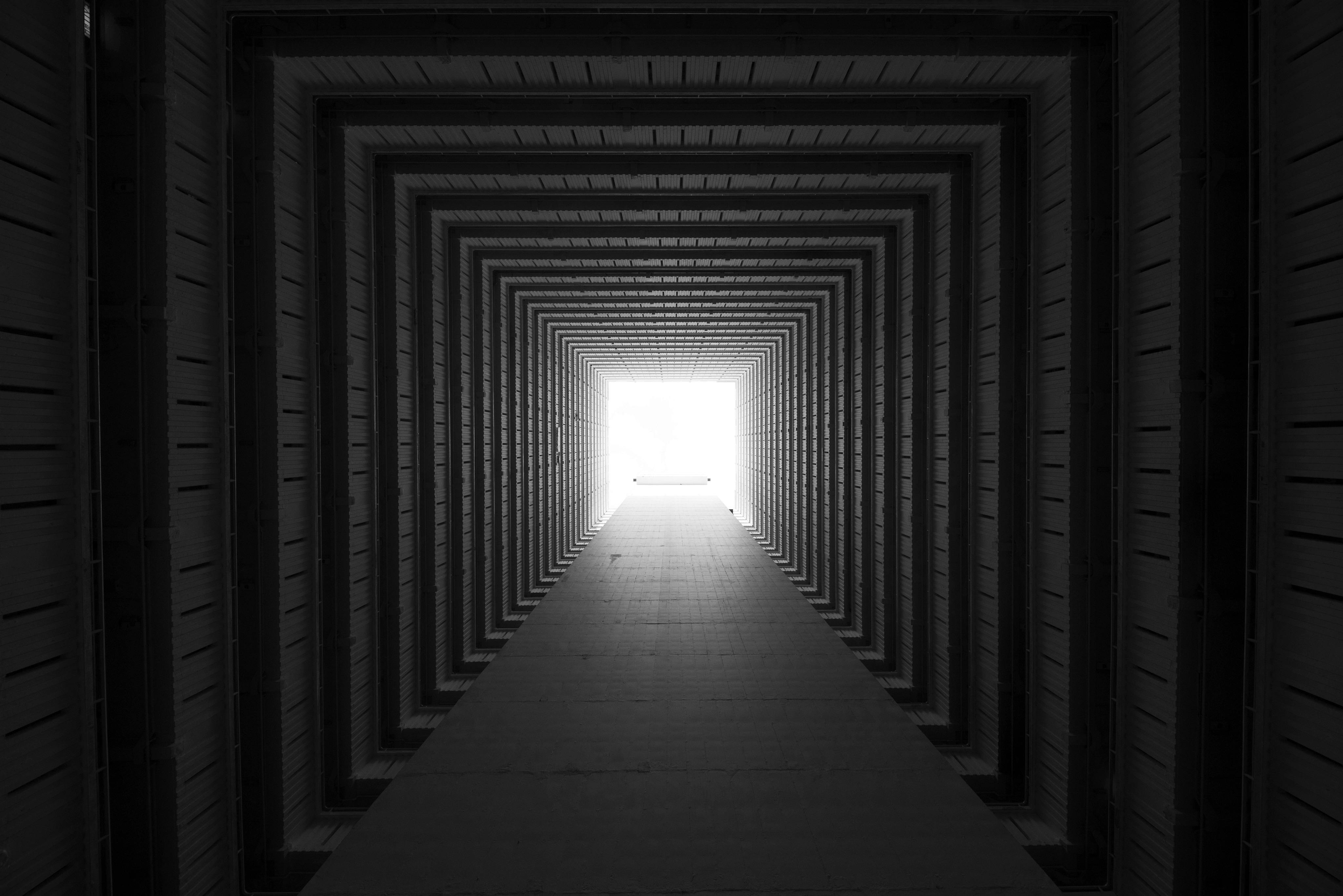 Black and white photo looking up through a square atrium with symmetrical repetitive balconies toward a bright sky.