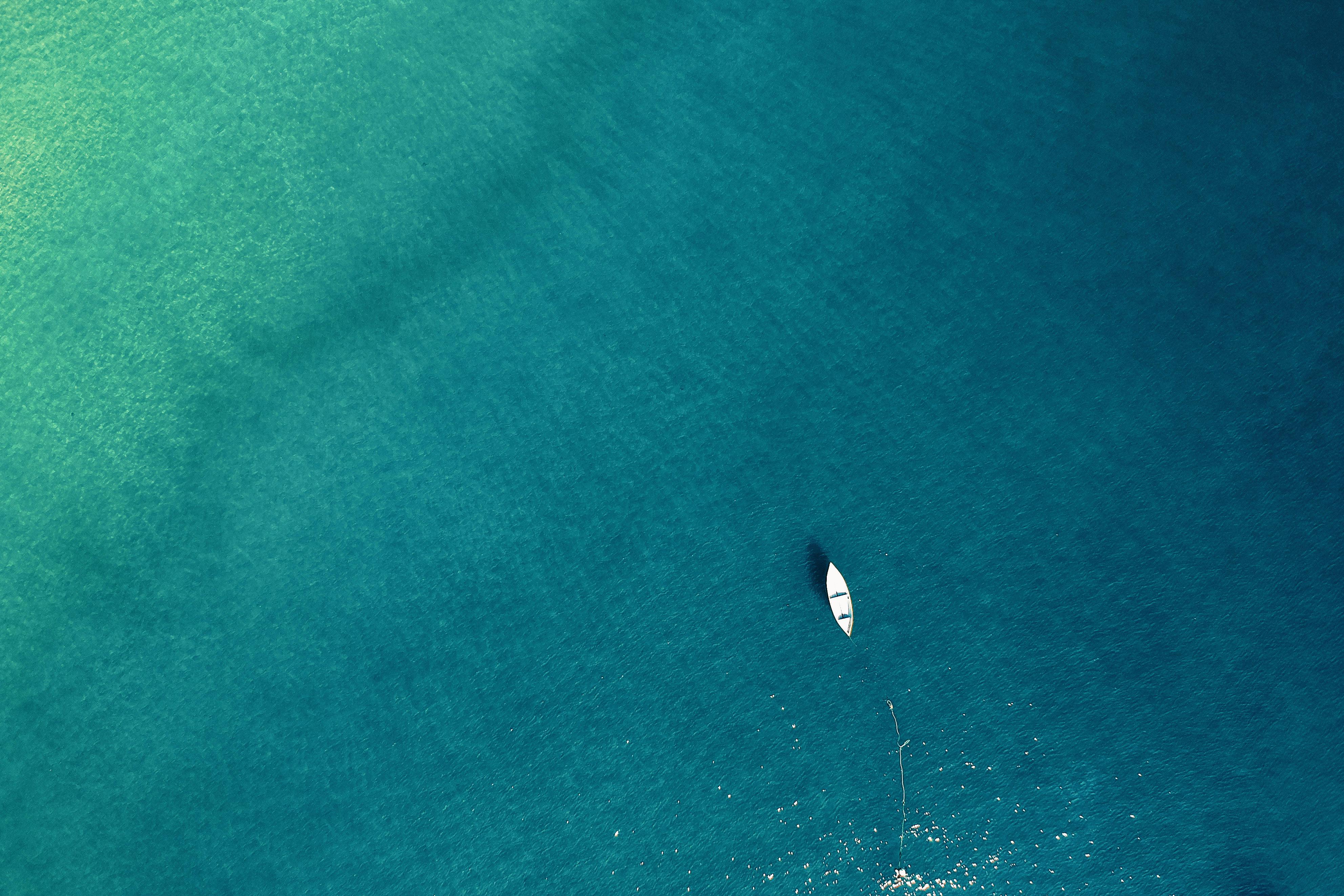 A small white boat floating alone on clear turquoise ocean water, seen from above.