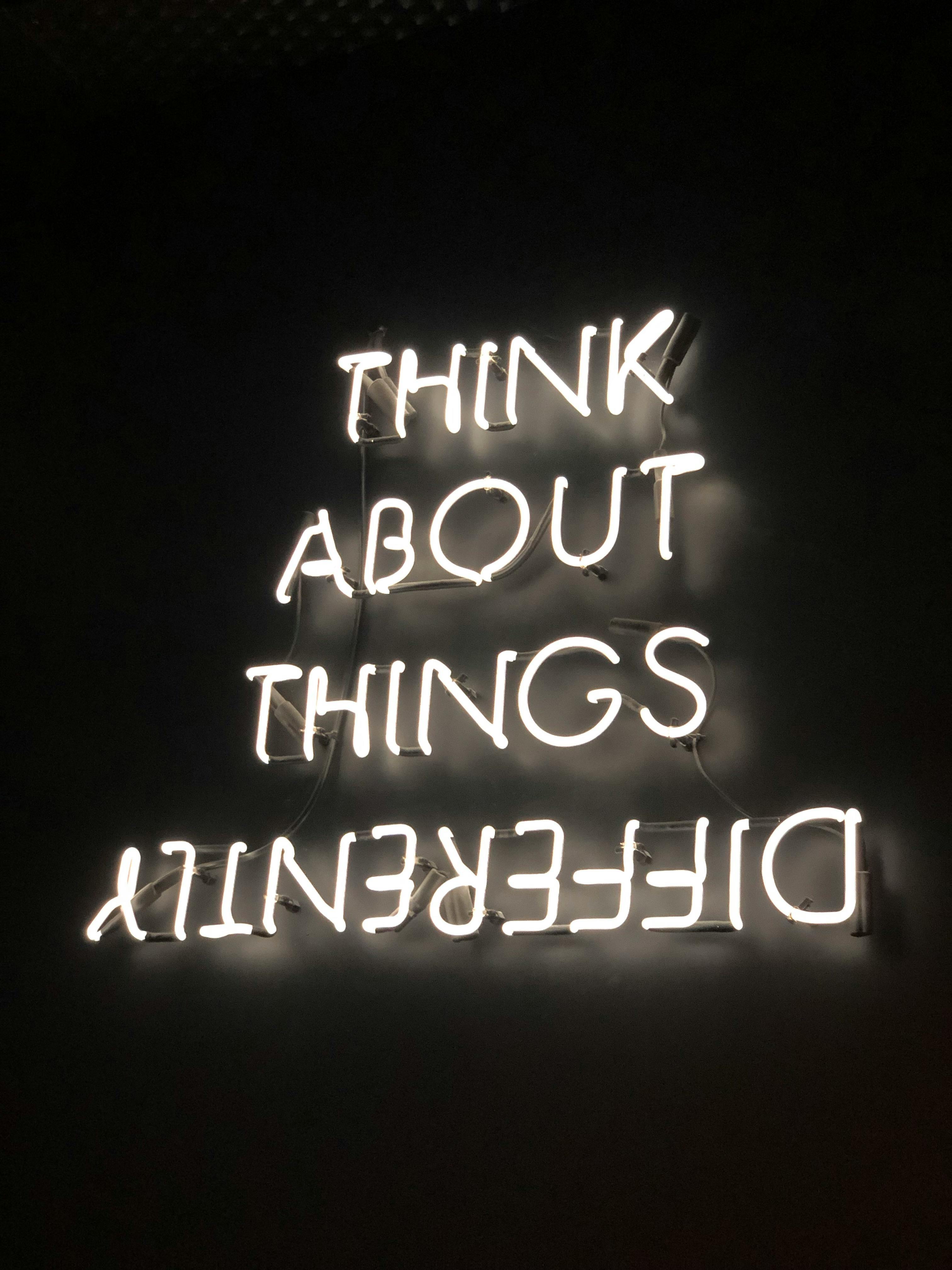 White neon sign reading 'THINK ABOUT THINGS DIFFERENTLY' on a black background, with 'DIFFERENTLY' displayed upside down.