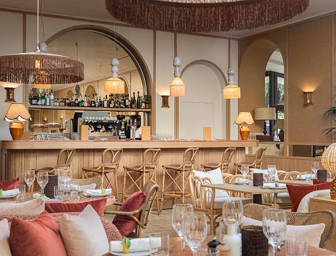 Intérieur d'un restaurant élégant avec tables dressées, chaises en rotin, grand bar en bois et lampes suspendues décoratives.