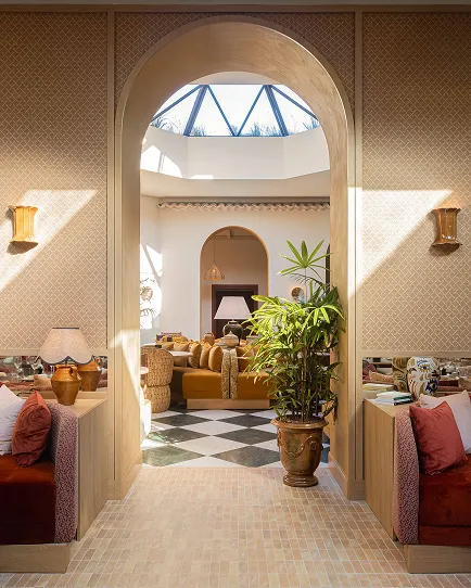 Elegant interior with wooden arch leading to a bright living room decorated with mustard sofas, a large potted plant, and a triangular glass ceiling.