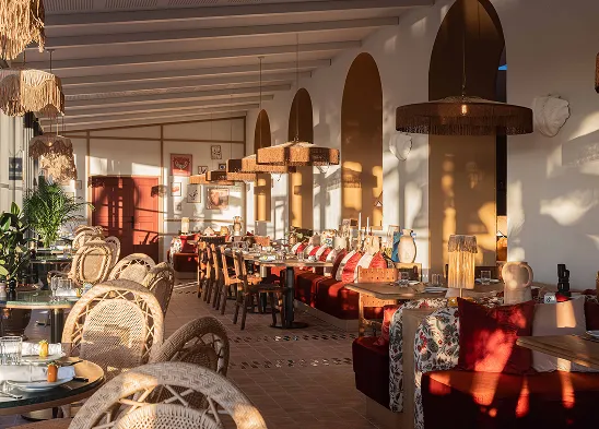 Stylish dining room with wicker chairs, large windows, rattan pendants, and sunlight brightens the room.
