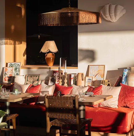 Living area with red and white sofa, matching cushions, wooden table, lamps, and decorative artwork illuminated by warm natural light.
