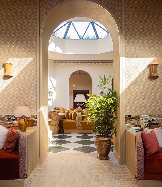 Bright entrance with wooden arch leading to a living room decorated with an orange sofa, large potted plant, lamps and black and white checkerboard flooring.