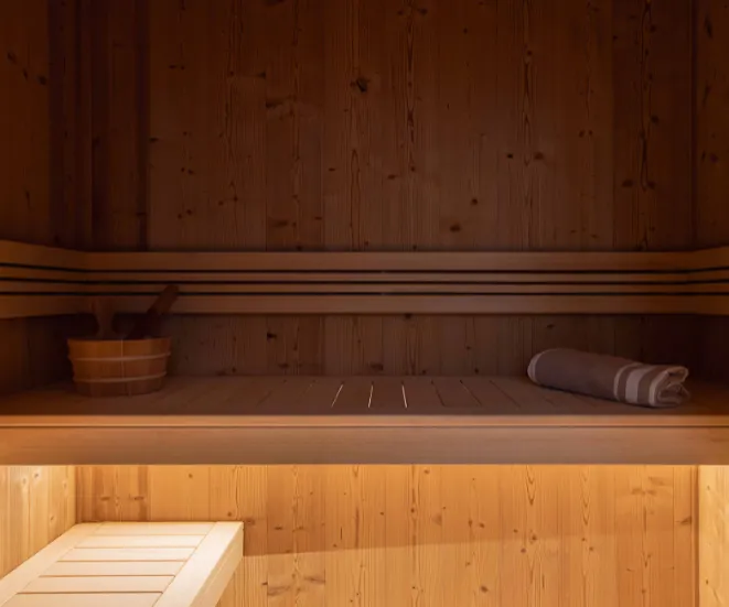 Intérieur d'un sauna en bois avec un seau, une louche et une serviette roulée sur une banquette.