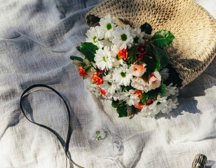Bouquet of white and orange flowers placed on a light fabric next to a woven straw hat.