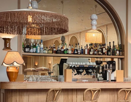 Light wooden bar counter, decorated with fringed lamps, with a large mirror and a wide selection of alcohol bottles.