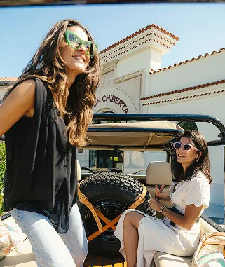 Deux femmes souriantes devant l’entrée de Maison Chiberta à Anglet avec véhicule et bagages
