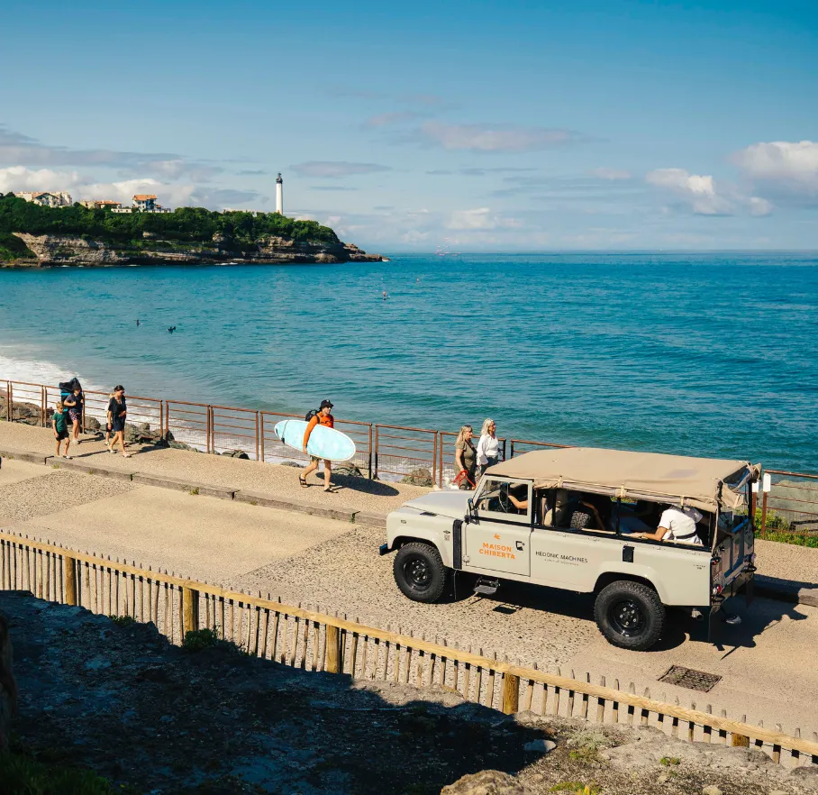 Surfeur avec planche marchant sur le front de mer à Anglet avec 4x4, océan et phare en arrière-plan