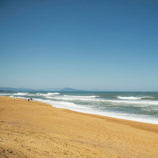 Plage de sable doré avec quelques personnes au bord de l'océan et ciel bleu clair.