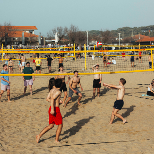 Jeunes jouant au volley-ball sur une plage sableuse sous un ciel clair.