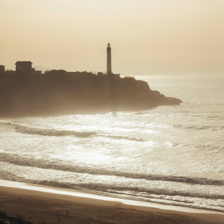 Phare au sommet d'une falaise surplombant une plage au coucher du soleil avec des vagues scintillantes.