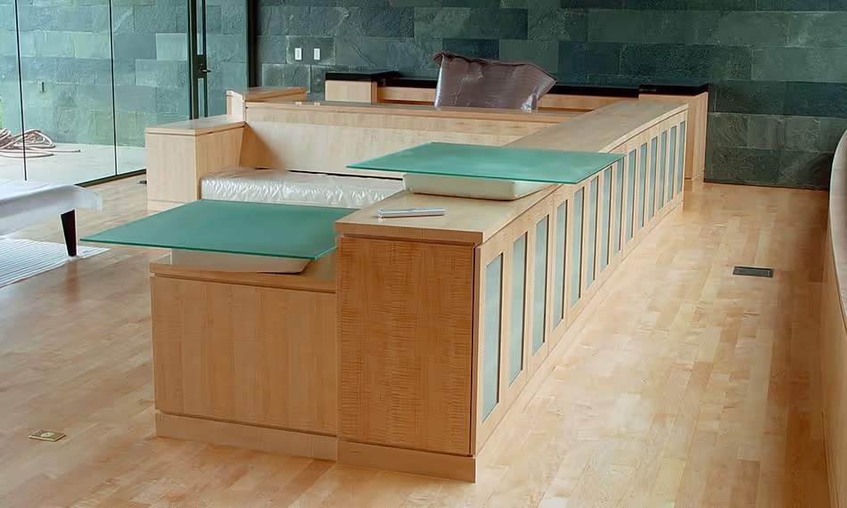 Modern living room with a large wooden U-shaped sectional sofa featuring built-in frosted glass shelves and green glass tables.