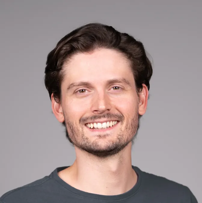 Porträt eines lächelnden Mannes mit kurzem Bart, kurzem schwarzen Haar und schwarzen Ohrsteckern vor weißem Hintergrund.