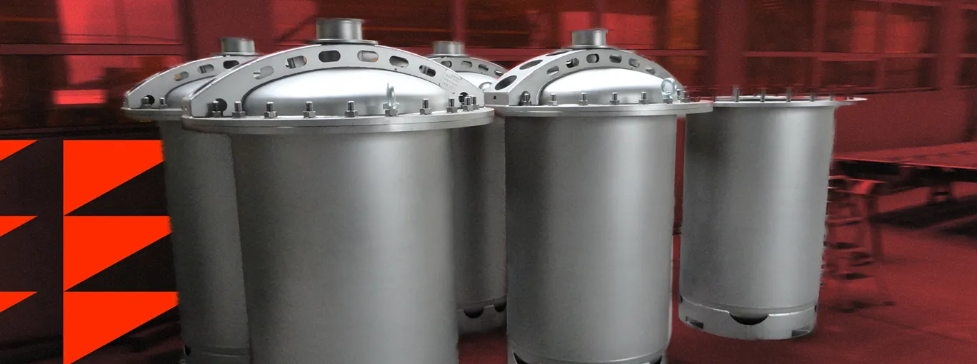 Skupina šesti velkých kovových průmyslových nádoba nebo filtrů se šroubovacími víky ve výrobním prostředí s červeným pozadím.